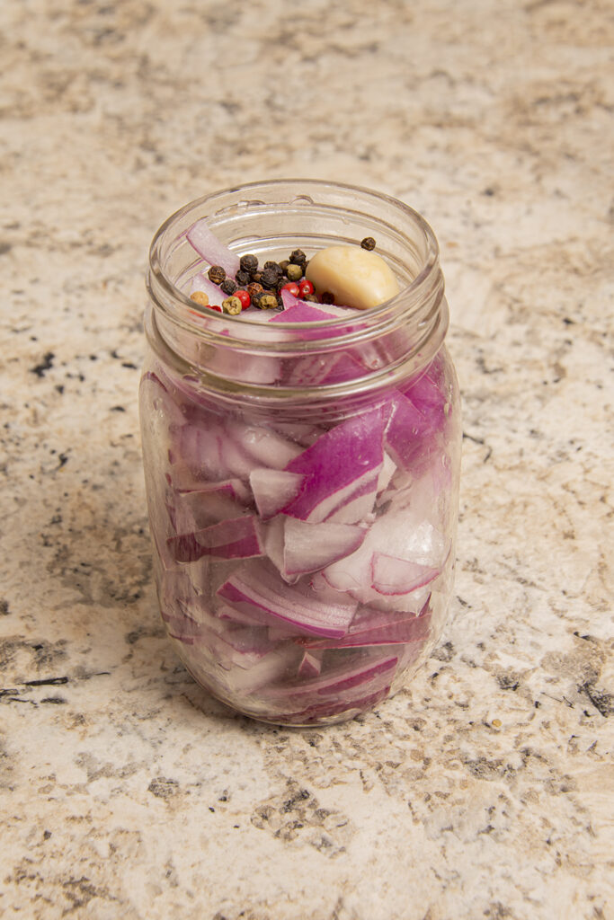 Red onions chopped and placed in a 12oz Mason jar with peppercorns and garlic added.