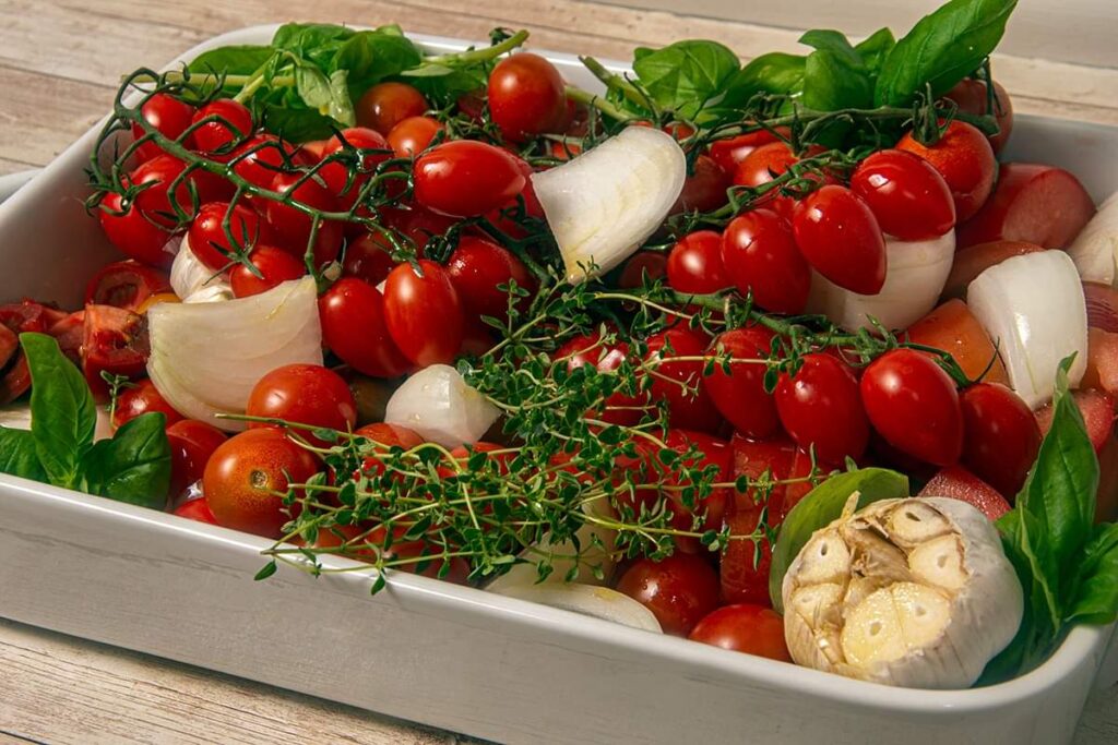 Place all tomatoes, garlic, onion, basil and thyme into a baking dish a top with olive oil.
