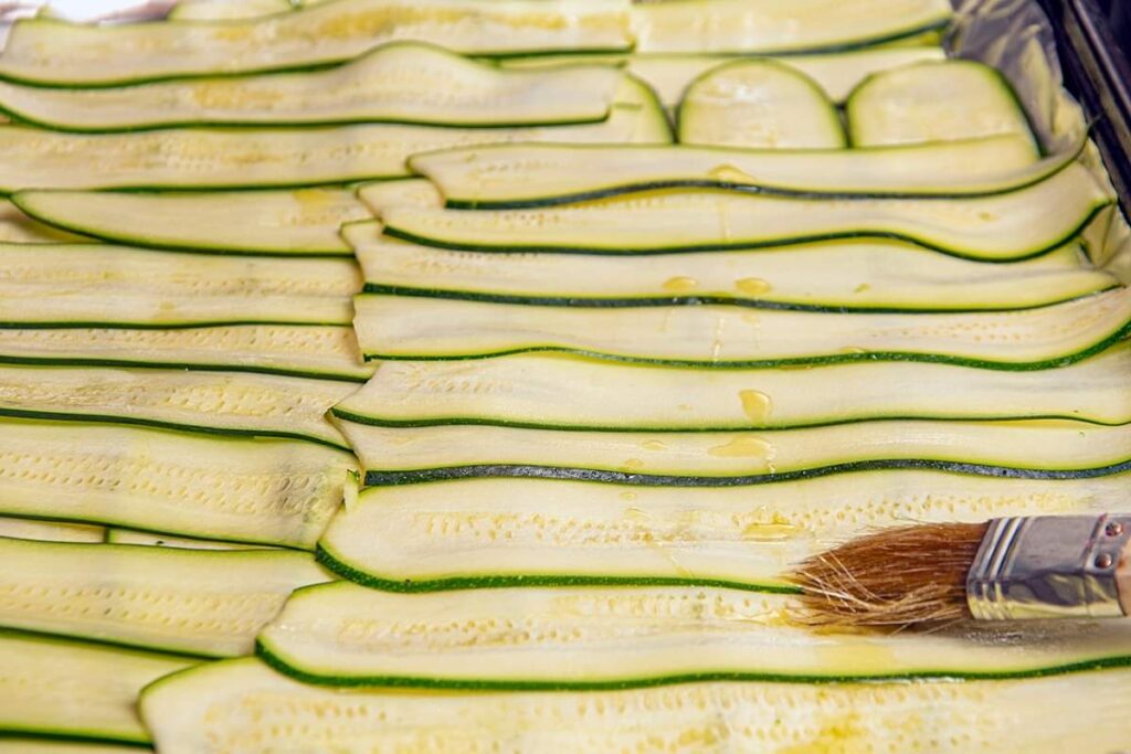 Sliced zucchini brushed with olive oil on a foiled lined baking sheet. 